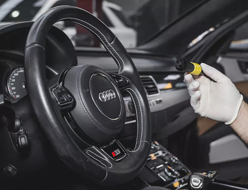 A Man Holding the Car Polish Brush infront of Audi car Steering