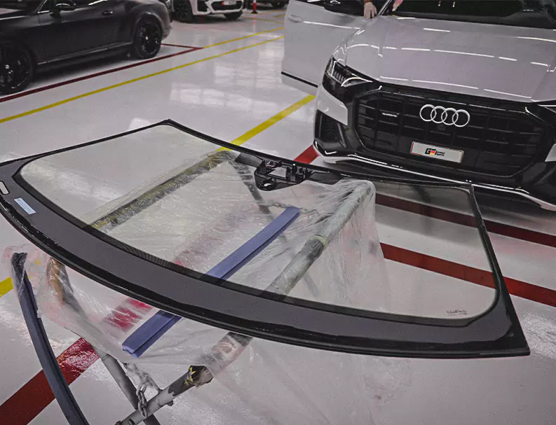 A Windscreen on stand infront of white Audi Car